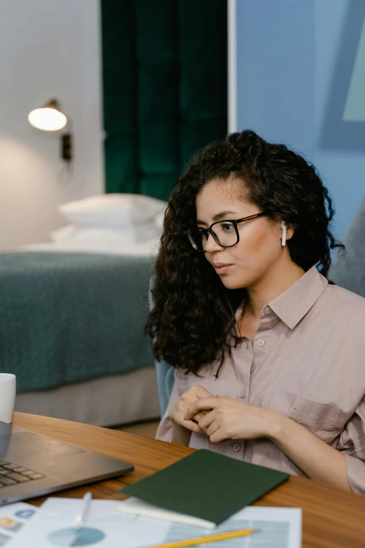 a woman sitting in front of a laptop computer, trending on pexels, renaissance, hotel room, wavy long black hair and glasses, pondering, curly haired