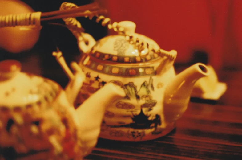 a tea pot sitting on top of a wooden table, a tilt shift photo, flickr, cloisonnism, yellow lanterns, redscale photography, very ornate, fan favorite