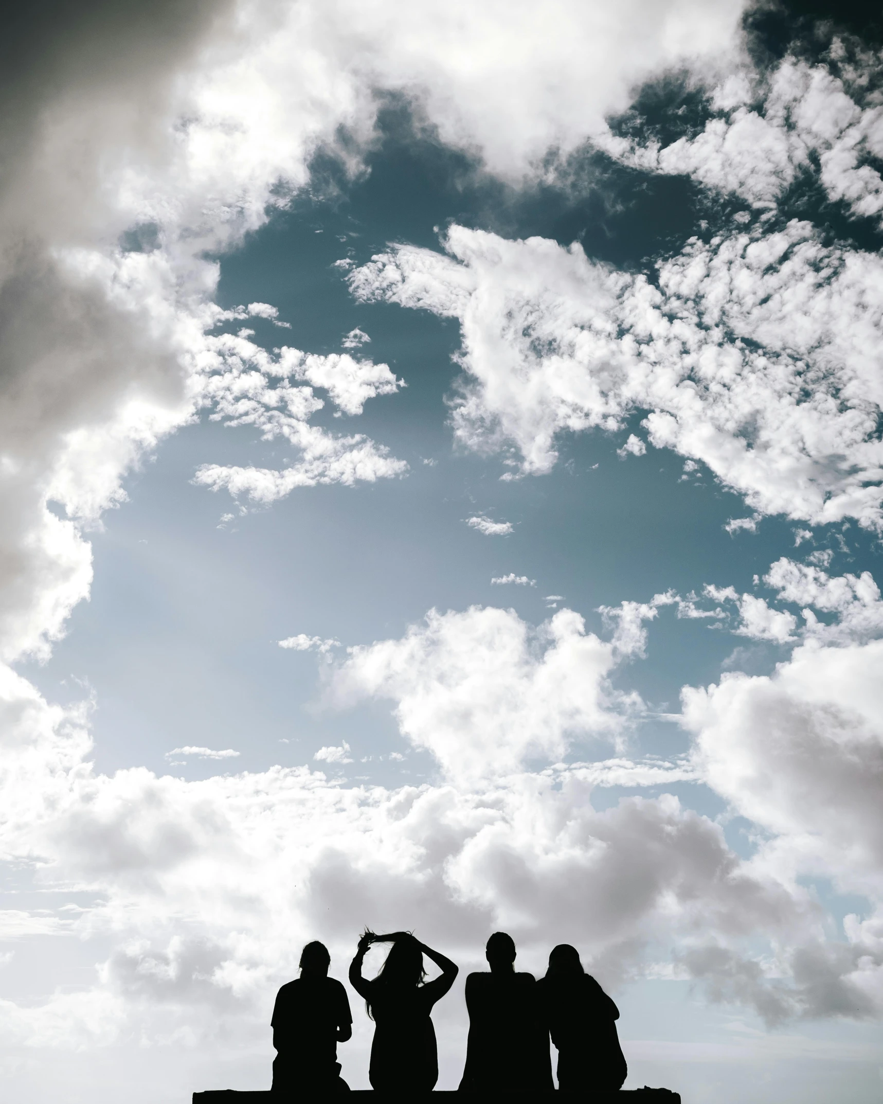 a group of people sitting on a bench under a cloudy sky, in the sky