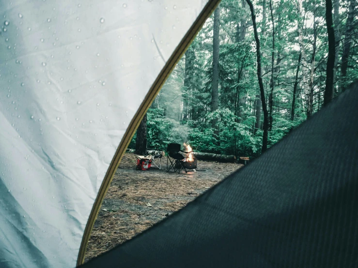 a person sitting at a table in a tent, a picture, unsplash contest winner, rainy outside, trees in the background, close up camera on bonfire level, curved perspective