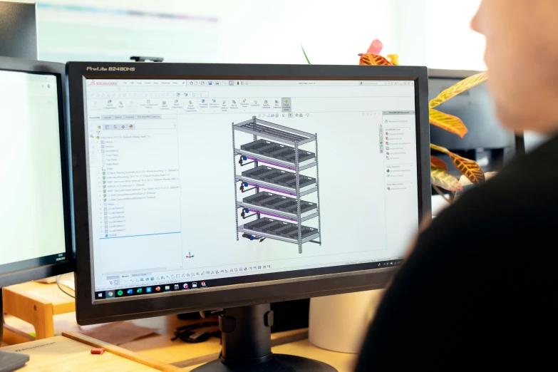 a man sitting at a desk in front of two computer monitors, a computer rendering, solidworks, rack, blurred photo, product design