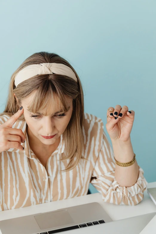 a woman sitting at a table in front of a laptop, scratching head, photo of a hand jewellery model, wearing a headband, wearing stripe shirt