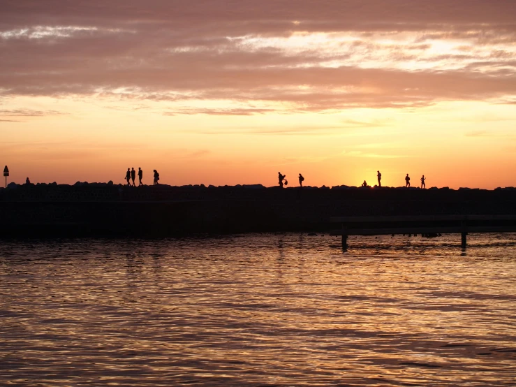 a group of people standing on top of a body of water, by Colijn de Coter, pexels contest winner, evening sunset, fishing, big island, walking to the right