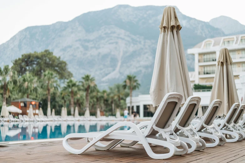 a row of lounge chairs sitting on top of a wooden deck, by Emma Andijewska, pexels contest winner, carrara marble, white and gold robes, mount olympus, palm trees in the background