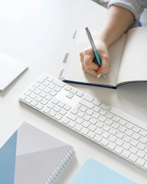 a person sitting at a desk with a keyboard and a notebook, white and pale blue, flatlay, background image, multiple stories
