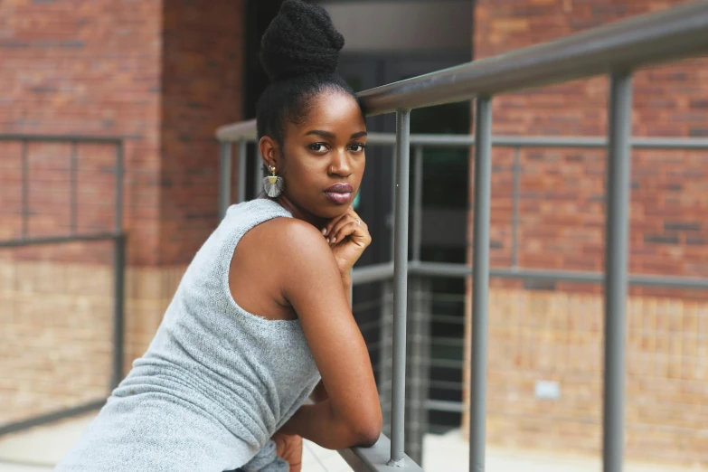 a beautiful young woman leaning against a railing, by Lily Delissa Joseph, pexels contest winner, happening, topknot, with grey skin, she is wearing a black tank top, ( ( dark skin ) )