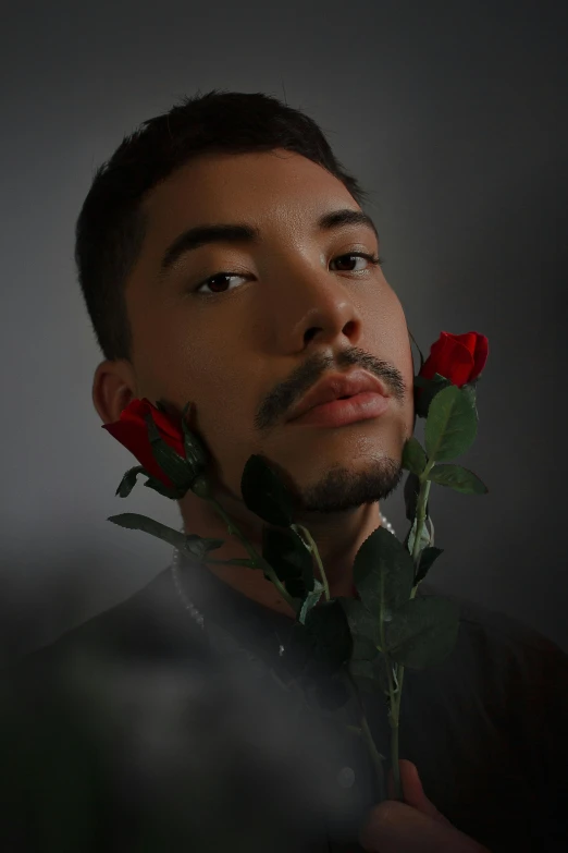 man holding two red roses to his face with dark background