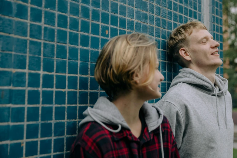 a man and a woman standing in front of a blue wall, an album cover, by Emma Andijewska, trending on unsplash, red haired teen boy, 15081959 21121991 01012000 4k, lesbians, blond boy