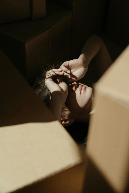 a woman laying on the ground in a box, inspired by Elsa Bleda, pexels contest winner, conceptual art, frustrated face, cardboard, light and dark, made of cardboard