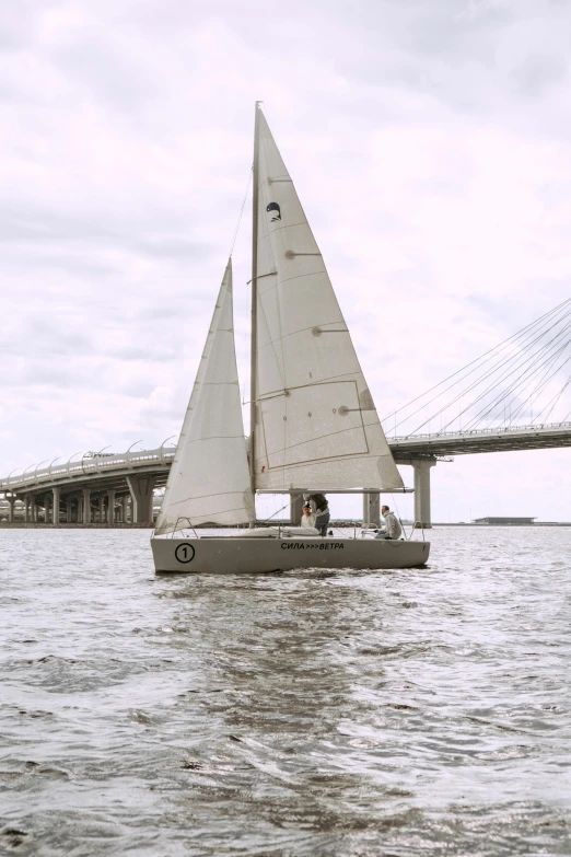 a small sail boat in the water by a bridge