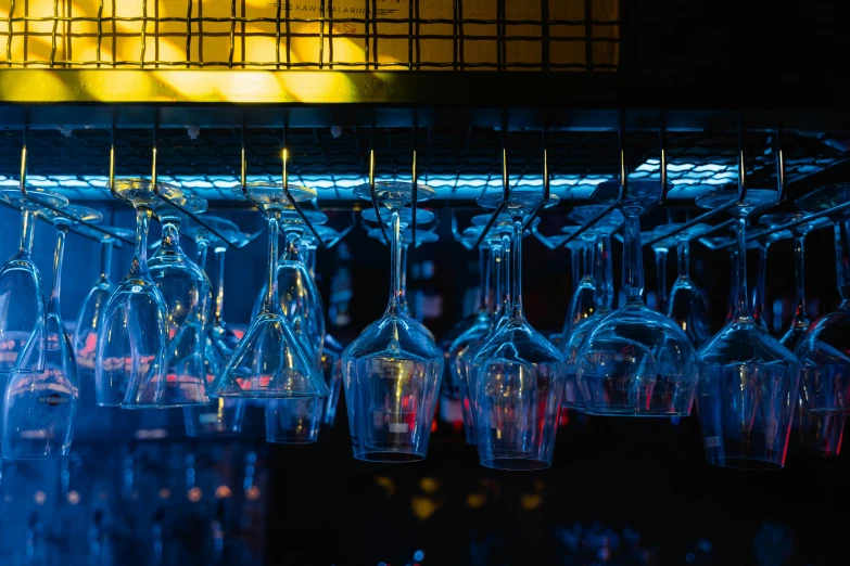 a bunch of wine glasses hanging from a rack, unsplash, happening, blue neon details, in a strip club, nightcap, thumbnail