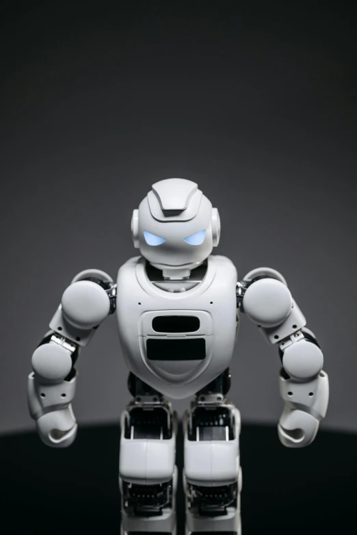 a close up of a toy robot on a table, looking towards the camera, grey, < full body robot >, cybertech