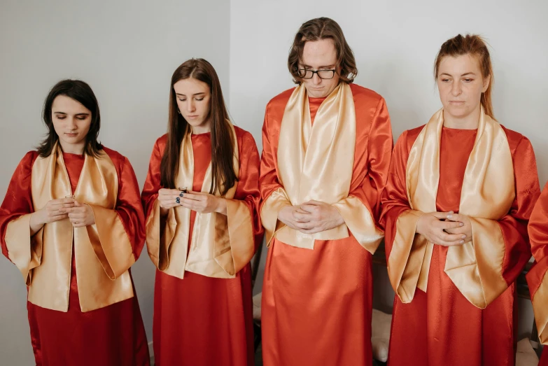 a group of women standing next to each other, an album cover, inspired by Petrus Christus, trending on unsplash, gutai group, orange robe, blessing hands, satin, holy ceremony