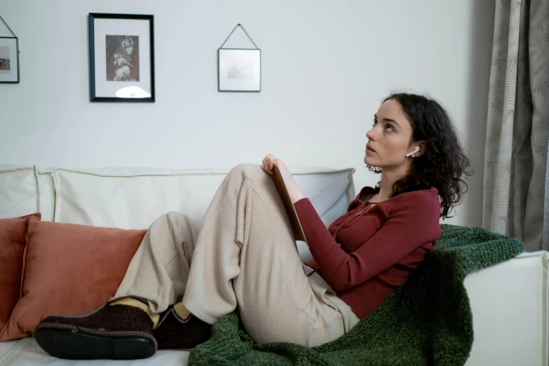 a woman sitting on a couch reading a book, inspired by Balthus, trending on pexels, with head phones, brown, wearing a tracksuit, side profile shot