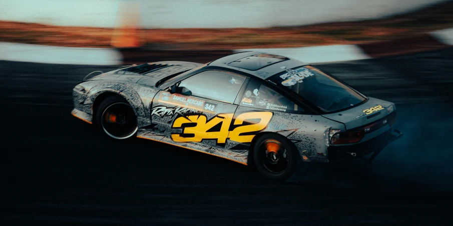 a grey and yellow sports car with numbers on it driving through a race track