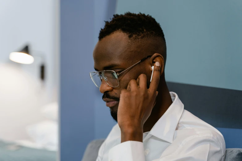 a man sitting on a couch talking on a cell phone, inspired by Barthélemy Menn, trending on pexels, realism, earbuds jewelry, professional profile picture, ( ( dark skin ) ), glasses without frames