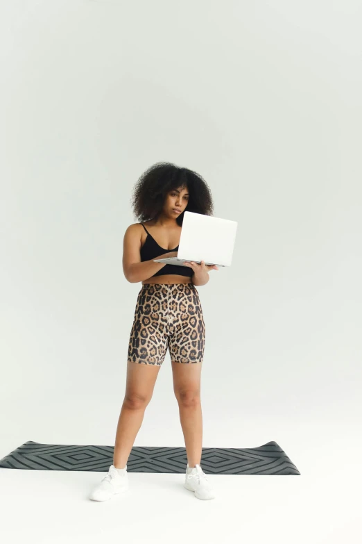 a woman standing on a yoga mat using a laptop, by Carey Morris, trending on pexels, happening, black boy shorts, full body with costume, wearing animal skin clothing, curls on top