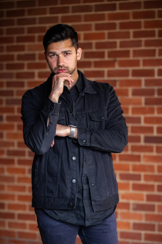 the young man is posing in front of a brick wall