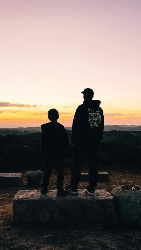 a couple of people standing on top of a rock, during a sunset, profile image, trending on r/streetwear, father figure image