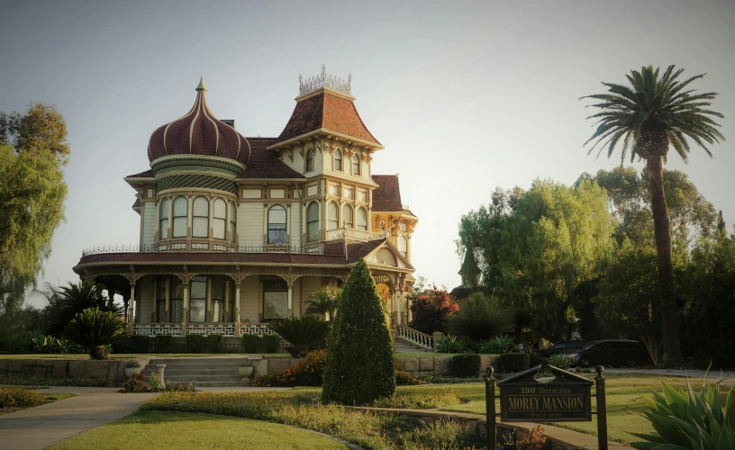 a large victorian house sits next to palm trees and a grassy walkway