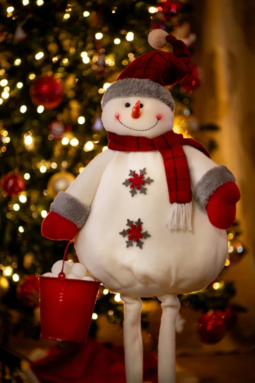 a large snowman with a red hat and scarf standing next to a christmas tree