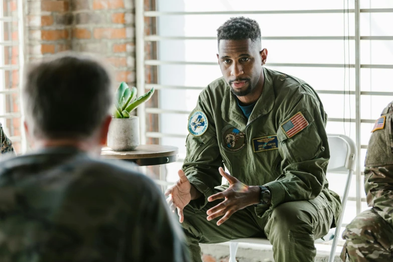 a man sitting in a chair talking to a group of soldiers, a portrait, pexels, advanced technology flight suit, aaron rodgers, jemal shabazz, military pilot clothing