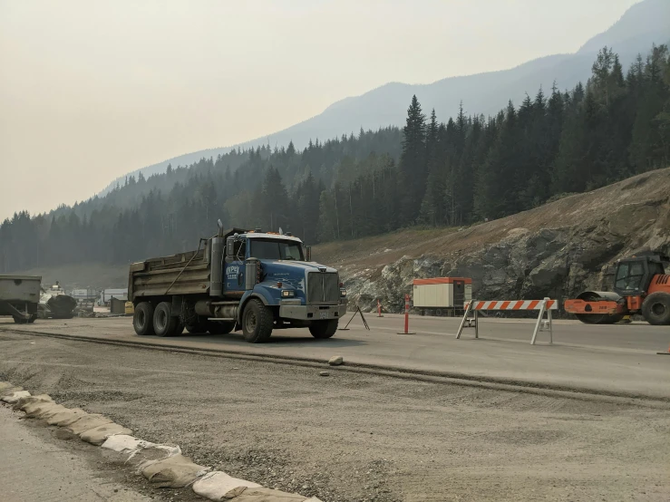 a large truck driving down a road next to a forest, happening, under construction, banff national park, avatar image, 2 0 2 2 photo