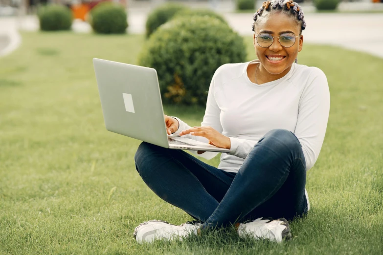 a woman smiling while she uses her laptop on the grass