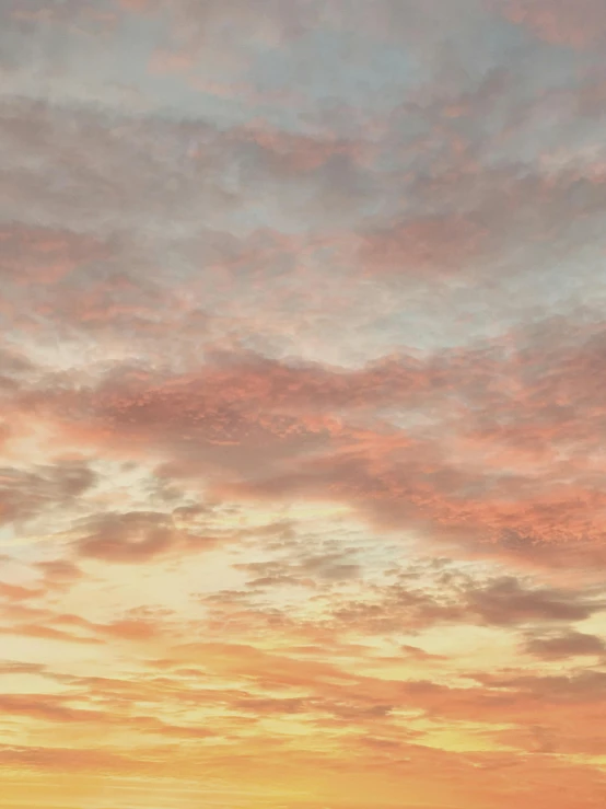 a man riding a surfboard on top of a sandy beach, by Carey Morris, pexels contest winner, romanticism, pink tinged heavenly clouds, panorama view of the sky, in shades of peach, ((sunset))