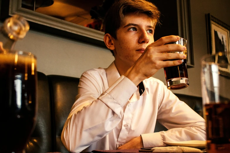 a man sitting at a table with a glass of beer, by Joe Bowler, unsplash, wearing a school uniform, tom holland, profile image, holding a drink
