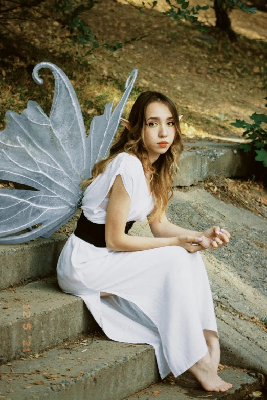 a woman in a white dress sitting on some steps, an album cover, inspired by Julia Pishtar, with two pairs of wings, zoe kazan, outdoor photo, young asian woman