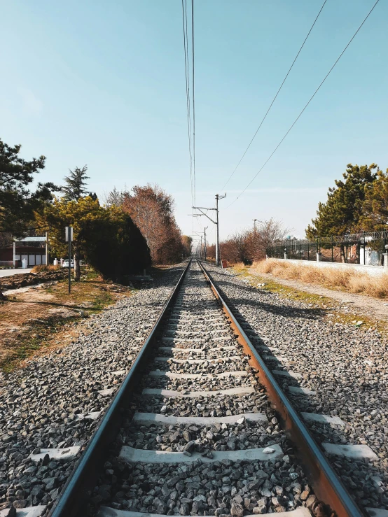 an empty railroad track with one section showing a single line and another in the distance with power lines on each side