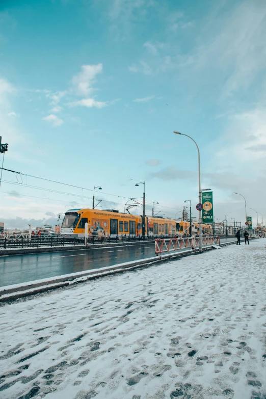 a yellow train traveling down train tracks next to a body of water, city snowing with a lot of snow, street tram, thumbnail, nordic