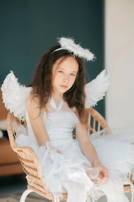a little girl in a white dress sitting on a chair, wearing angel halo, wearing a feather dress, for junior, medium-shot