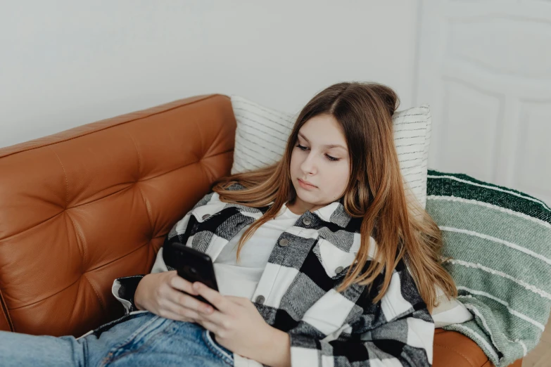 a woman sitting on a couch using a cell phone, trending on pexels, happening, portrait of white teenage girl, girl with brown hair, flattened, pokimane