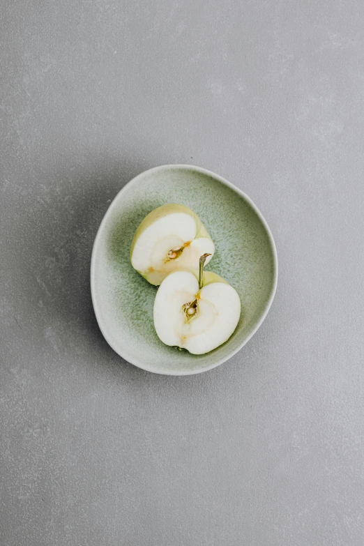 an apple cut in half on a plate, inspired by Maruyama Ōkyo, unsplash, minimalism, with celadon glaze, petite pear slim figure, 2 1 0 mm, with a soft