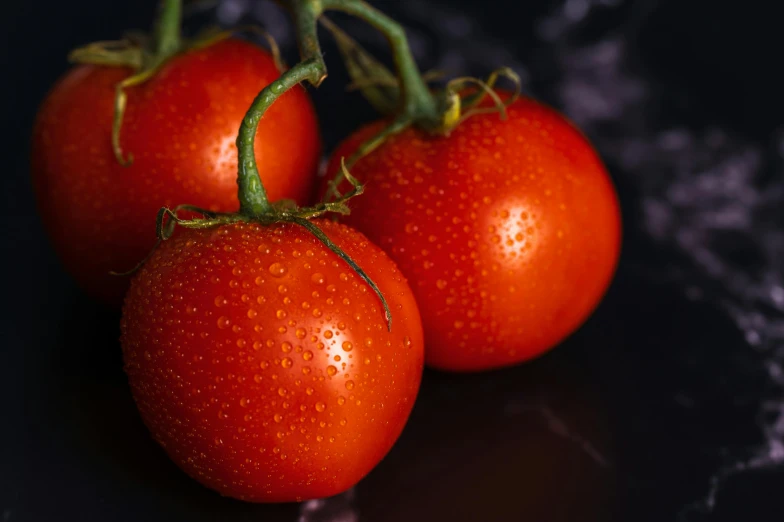 three red tomatoes sitting on top of a black surface, pexels contest winner, taken with sony alpha 9, uncrop, rain lit, vegetable