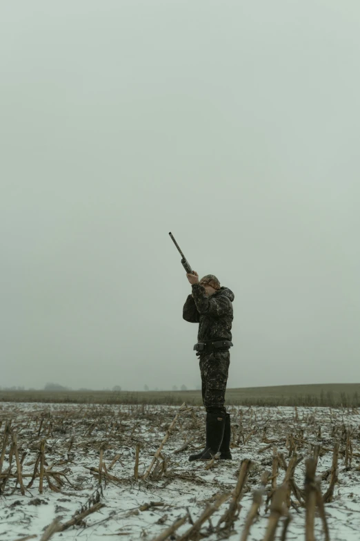 a man standing in a field with a gun, by Attila Meszlenyi, unsplash, duck, only snow in the background, prairie, low quality photo