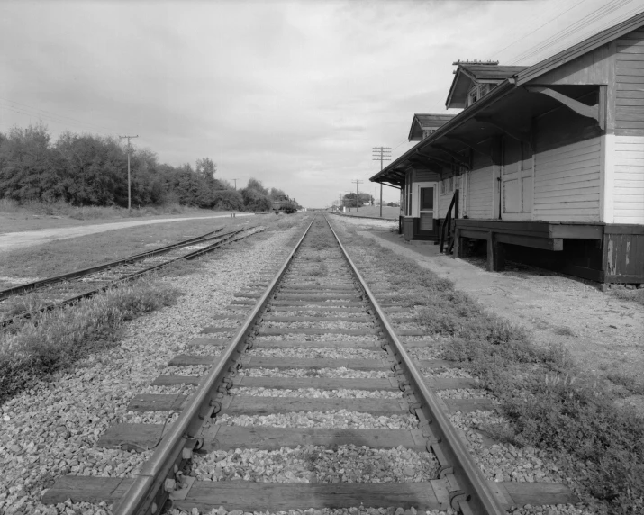 the tracks lead through a rural town, a small wooden building and trees on one side of the train track