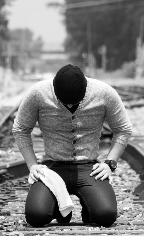 a black and white photo of a man kneeling on a train track, pexels, renaissance, clinically depressed, ripped clothing, islamic, resting head on hands