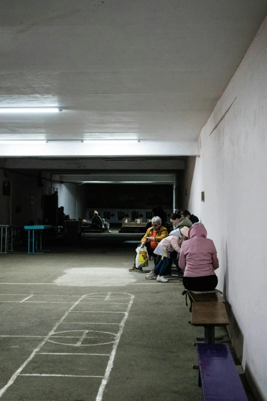 a group of people sitting on a bench in a parking garage, unsplash, quito school, inside a gang hideout, yuxiang chen, in line, low fi