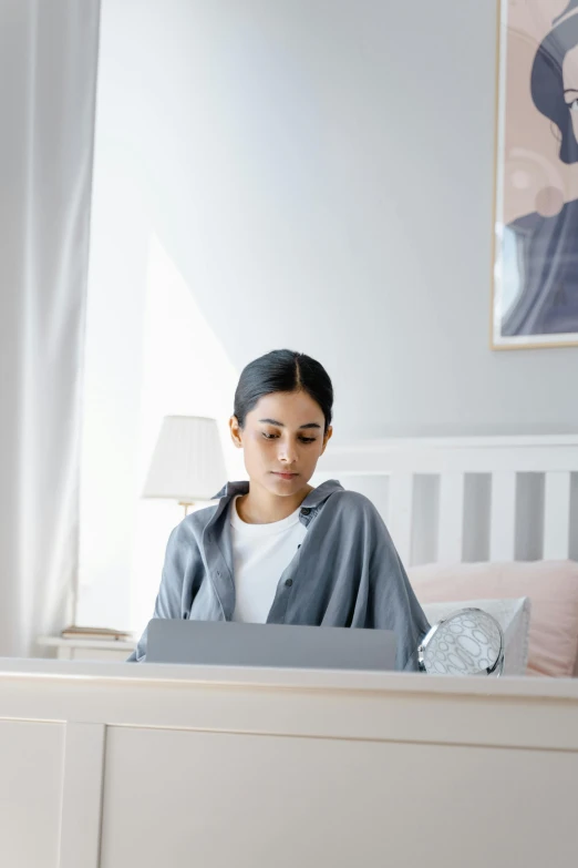 a woman sitting on a bed using a laptop, trending on pexels, wearing a grey robe, avatar image, student, concentration