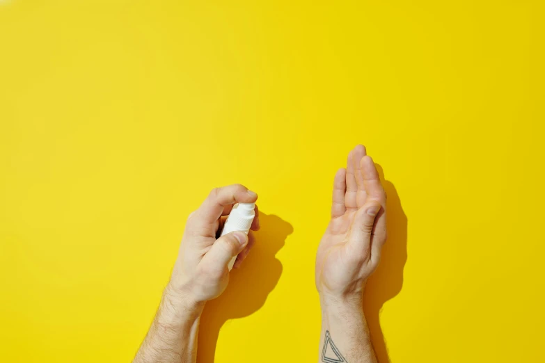 a person holding a bottle of hand sanitizer on a yellow background, inspired by Lubin Baugin, trending on pexels, chalk white skin, mana shooting from his hands, medium shot taken from behind, wolfy nail