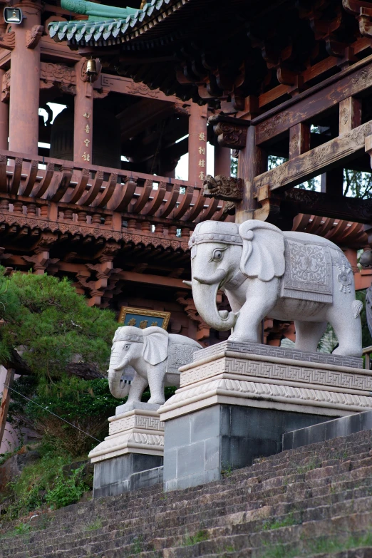 a couple of elephants that are standing in front of a building, a statue, inspired by Torii Kiyomitsu, shin hanga, large stones, exterior, nagasaki, brown