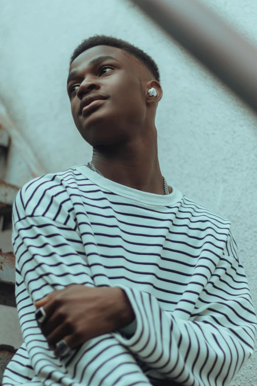 a man in a striped shirt leaning against a wall, trending on pexels, earbuds jewelry, ( ( dark skin ) ), wearing a white sweater, center of image