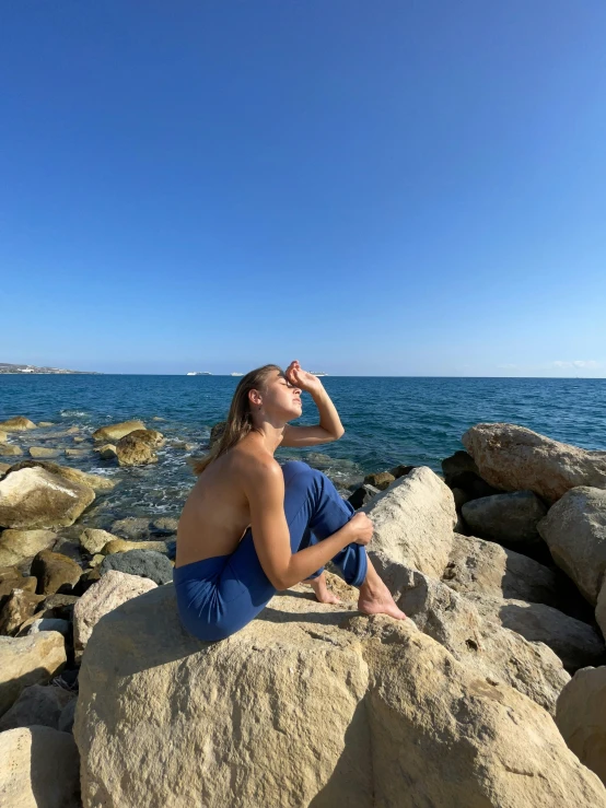 a woman sitting on top of a rock next to the ocean, profile image, sunbathed skin, agrigento, reddit post