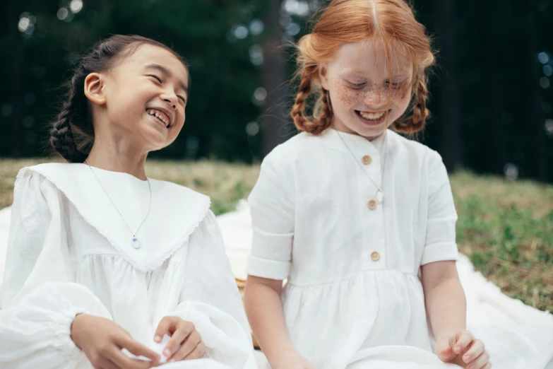 two little girls sitting next to each other on a blanket, inspired by Kate Greenaway, pexels contest winner, arts and crafts movement, earing a shirt laughing, white uniform, sadie sink, religious robes