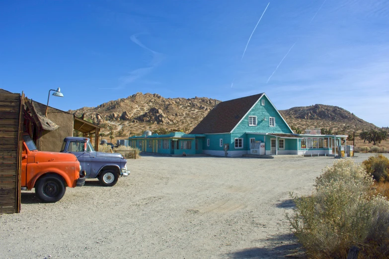 a couple of trucks parked in front of a building, by Arnie Swekel, pexels contest winner, retrofuturism, mojave desert, turquoise, square, panoramic shot