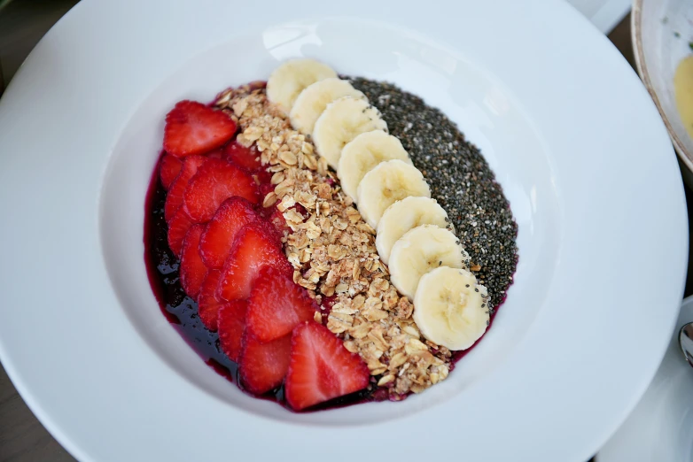 a white plate topped with fruit and granola, bowl filled with food