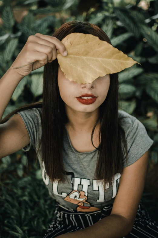 a woman holding a leaf over her face, pexels contest winner, wearing a t-shirt, beautiful asian girl, thick red lips, 33mm photo